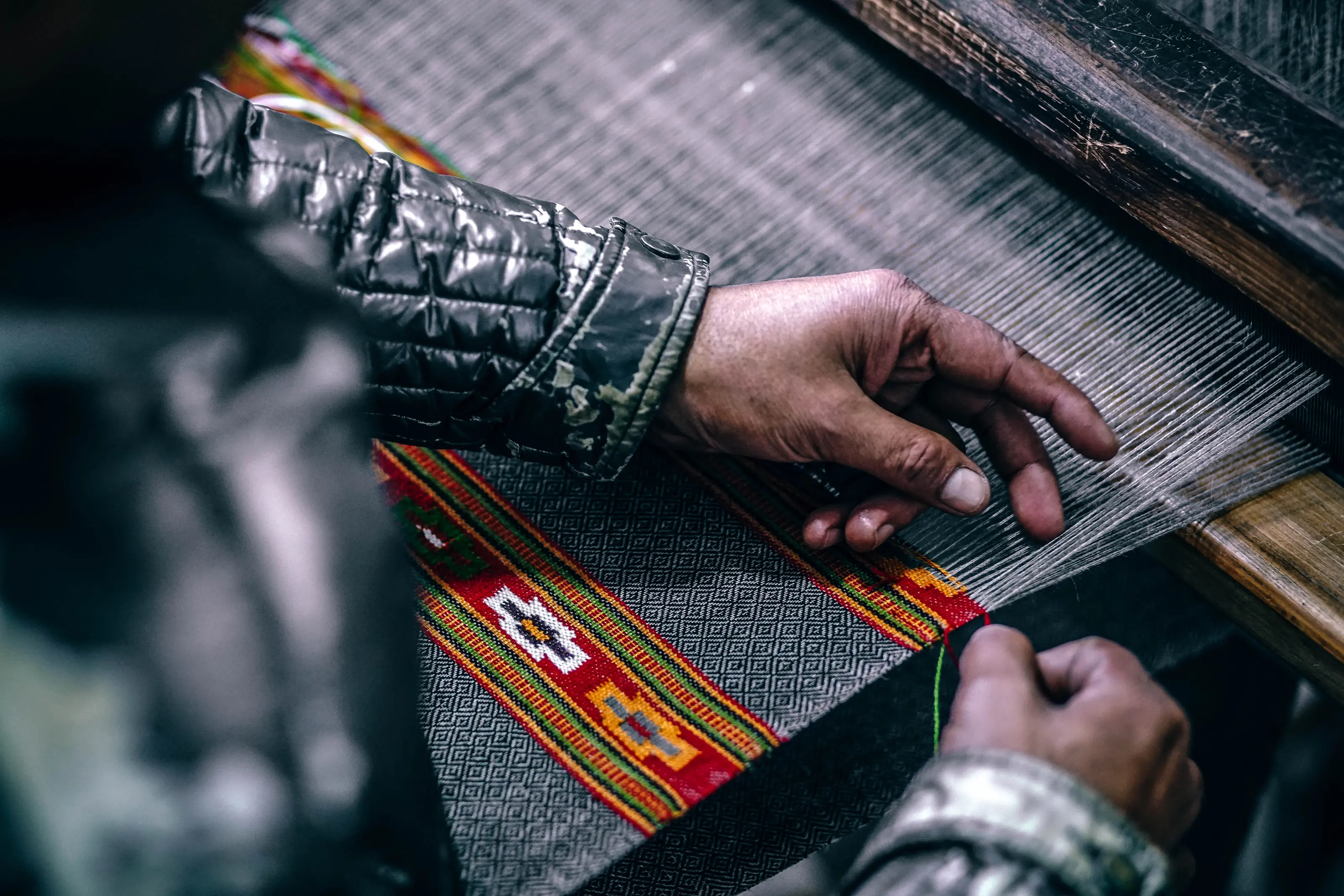 Hands guiding patterned cloth through a handloom in Manali